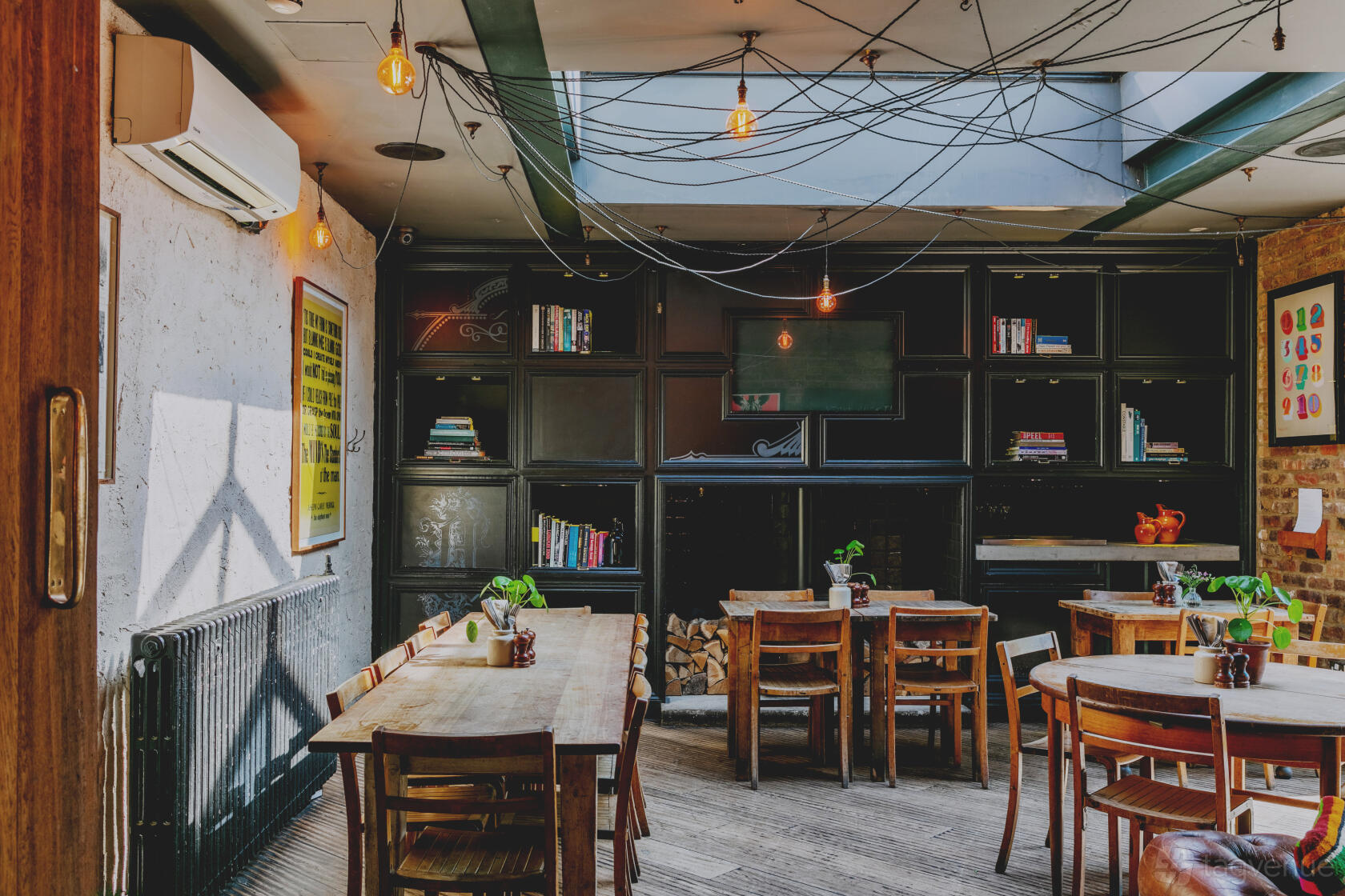An event space in a bar with bookshelves, exposed bulbs, and wooden tables at The Alice House Queen's Park.