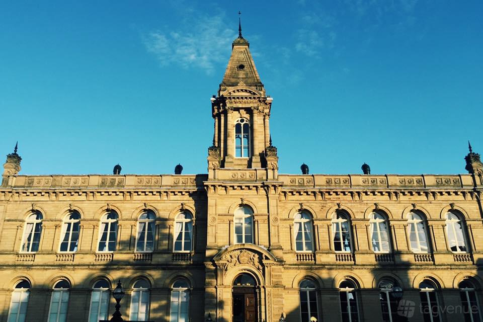 A historic stone event building with arched windows and a central clock tower at Victoria Hall Saltaire.