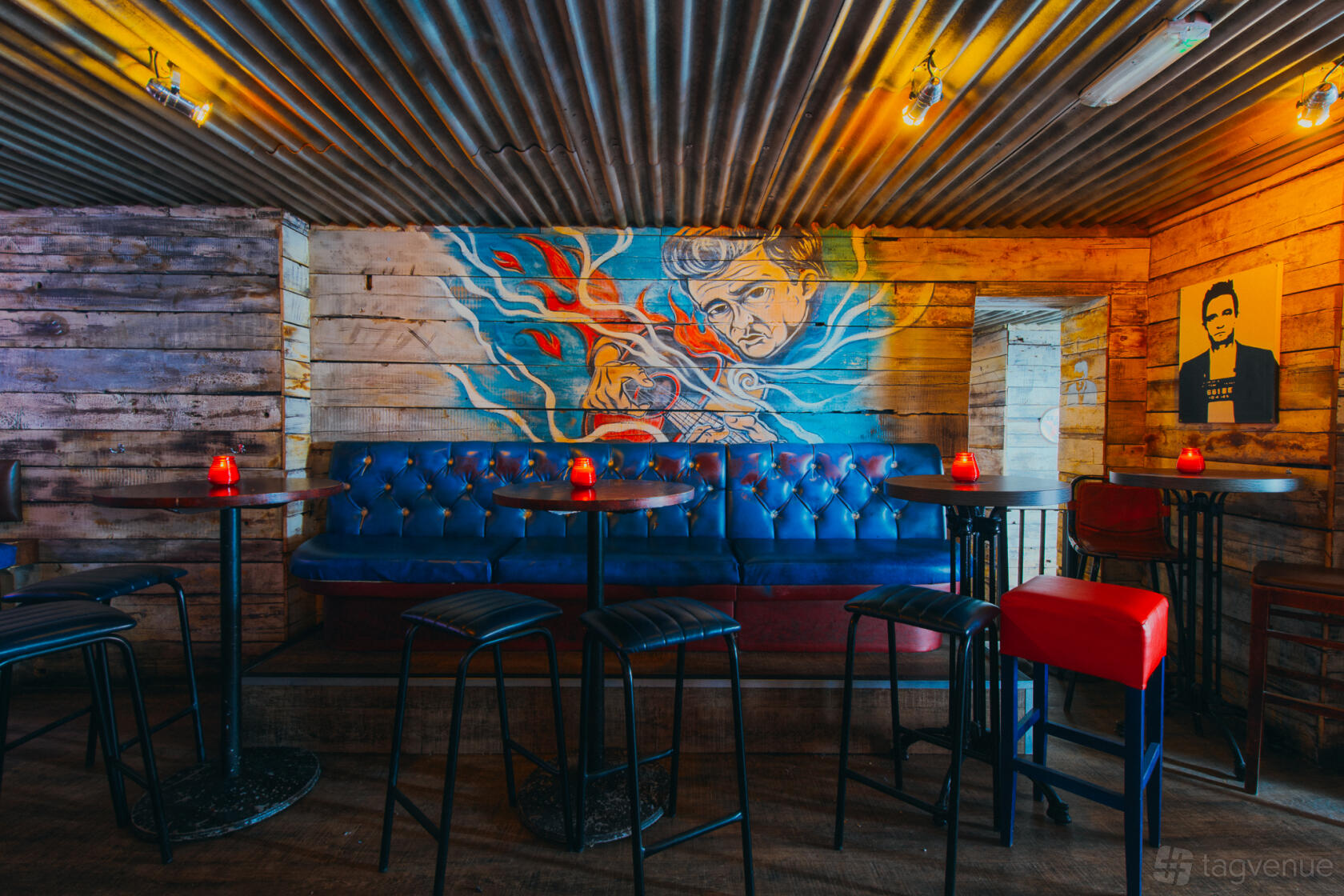 A function room in a bar with wood-paneled walls, a blue tufted bench, and a mural at Mean Eyed Cat Leeds.