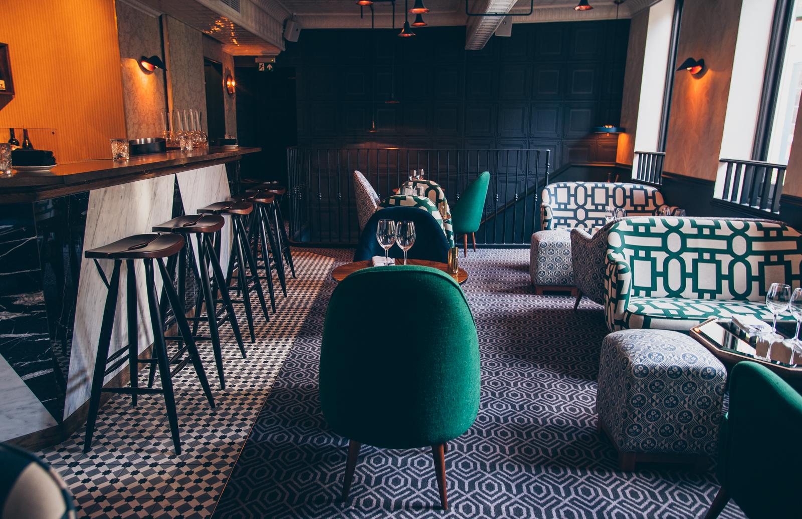 An event space in a bar with patterned armchairs, green upholstered chairs, and a marble-topped bar at La Compagnie.