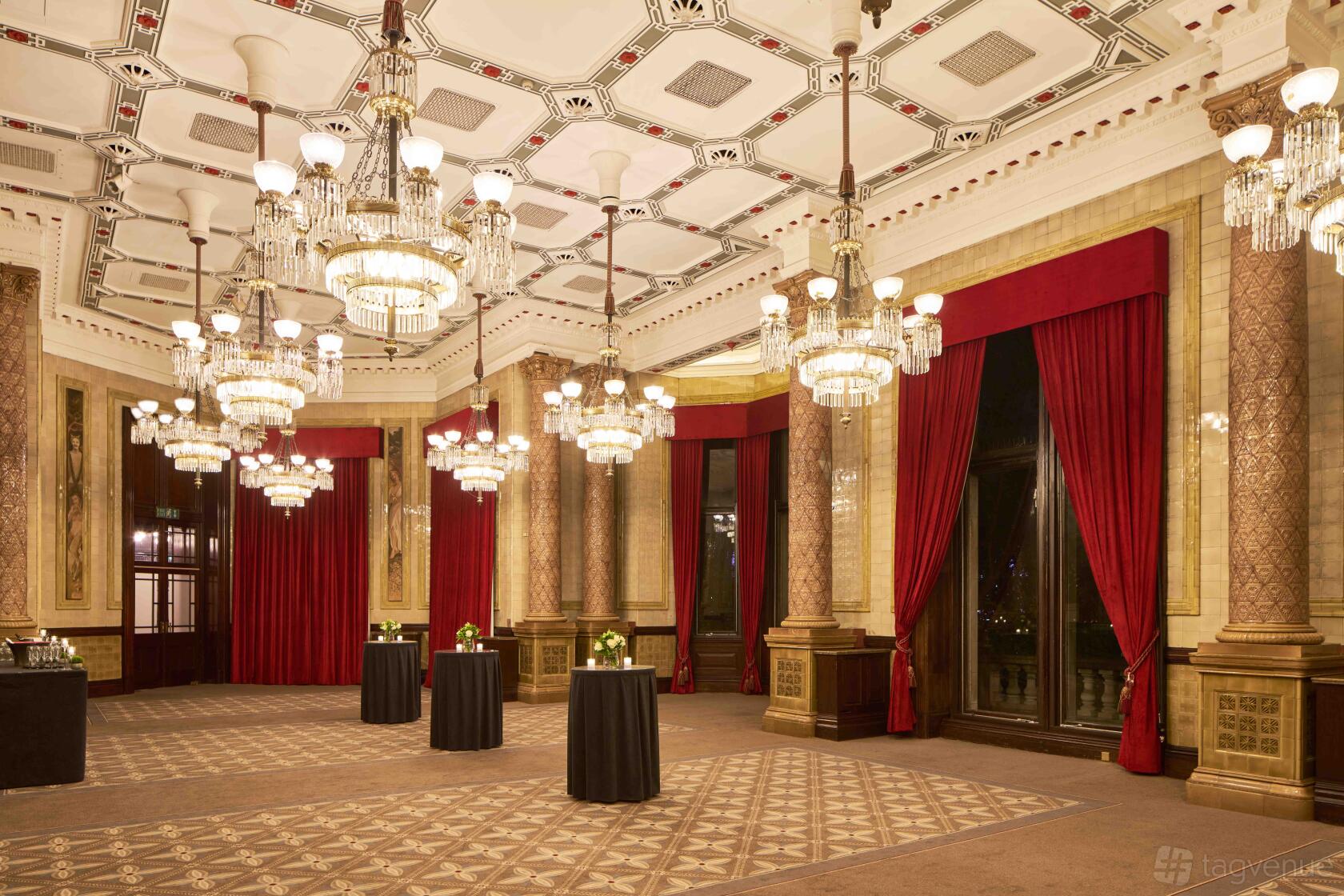 An event space in a hotel with ornate chandeliers, red velvet curtains, and decorative columns at The Royal Horseguards & One Whitehall Place.