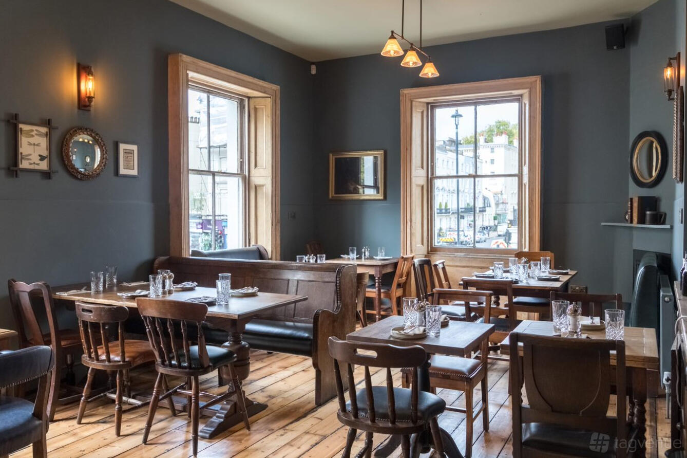 A pub dining room with wooden floors, mix of dark wood tables and chairs, and large sash windows at Marquis of Westminster.