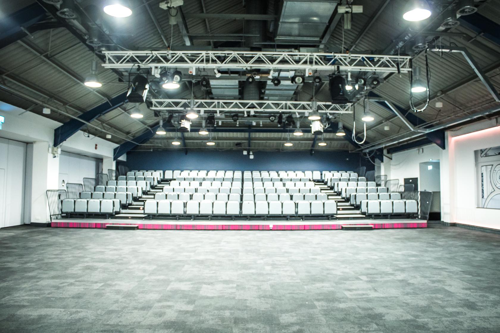 An auditorium with tiered seating, industrial-style ceiling, and overhead lighting at Business Design Centre.