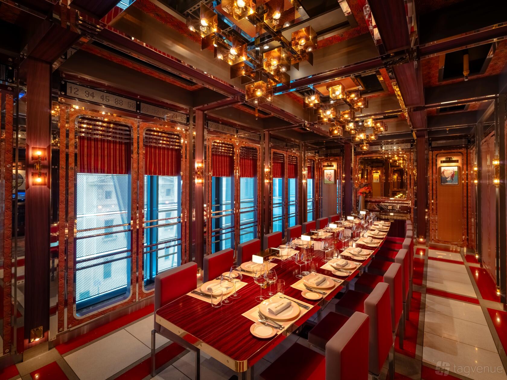 A private dining room with a long set table, red chairs, mirrored walls, and pendant lights at Bob Bob Ricard City.