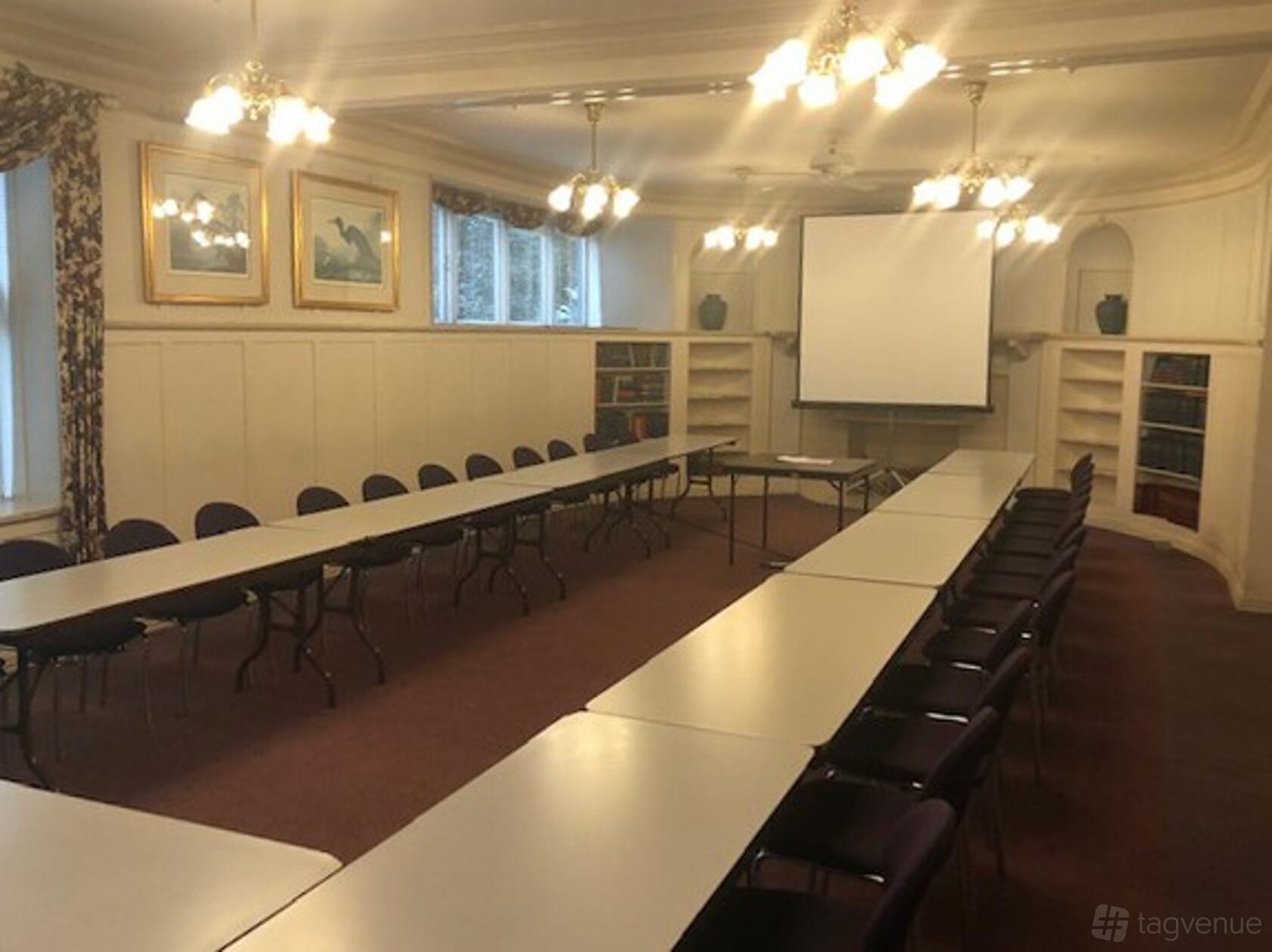 An event venue with U-shaped tables, cushioned chairs, and hanging ceiling lights at Preservation Park Ginn House.