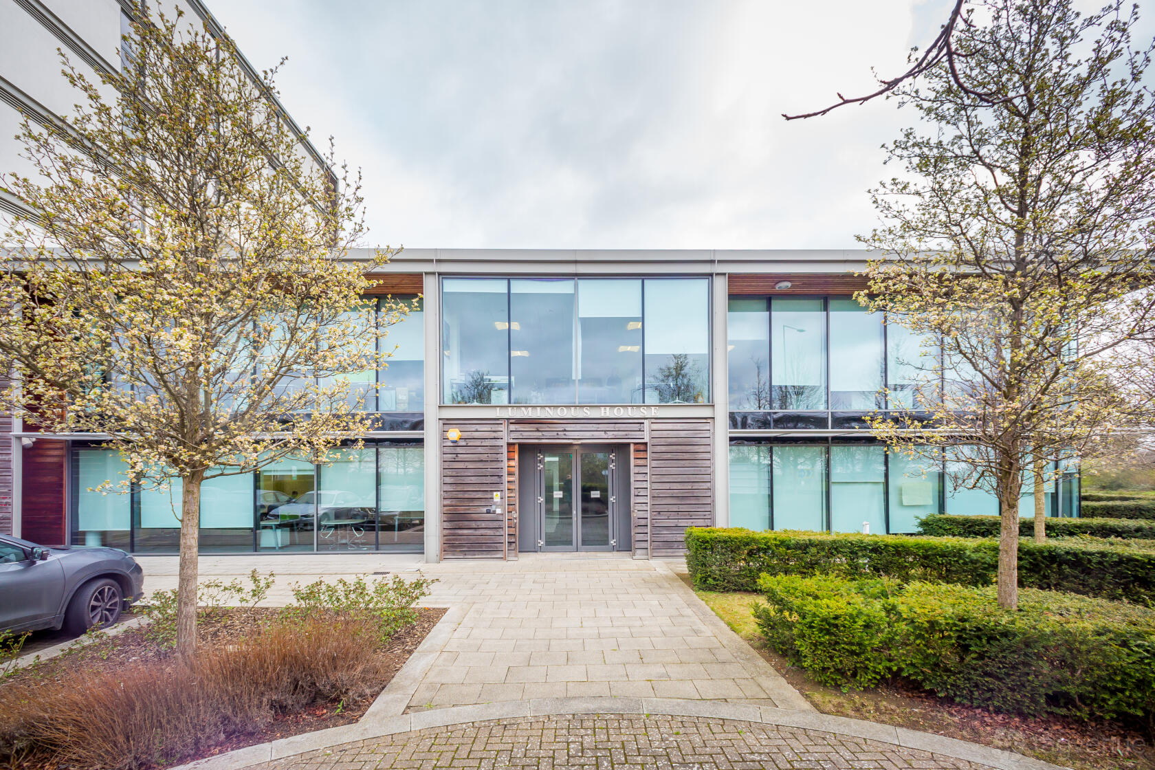 A meeting centre with large floor-to-ceiling windows, a glass entrance, and landscaped trees at Landmark: Luminous House, Milton Keynes.