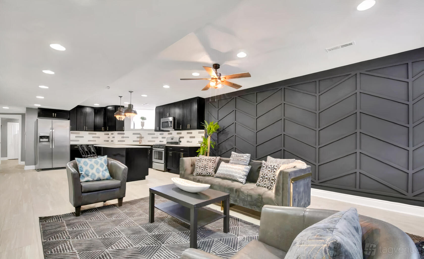 An apartment with a chevron accent wall, open kitchen, and lounge seating at The En Bronze.