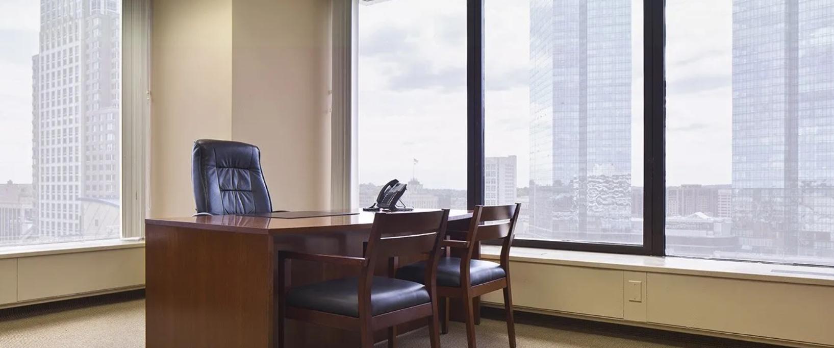 An office space with a wooden desk, executive chair, two guest chairs, and floor-to-ceiling windows at Coalition Space White Plains.