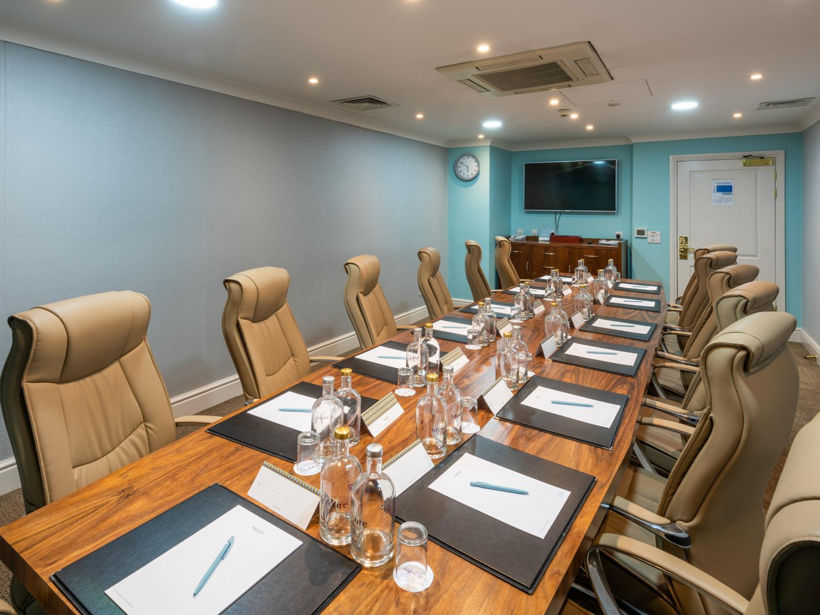 A hotel boardroom with leather chairs, notepads, water bottles, and a wall-mounted TV at Mercure Norton Grange Hotel and Spa.