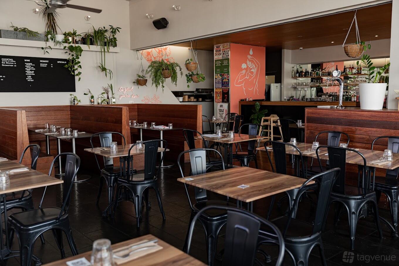A restaurant with wooden tables, black metal chairs, potted plants, and a bar counter at Yavanna.