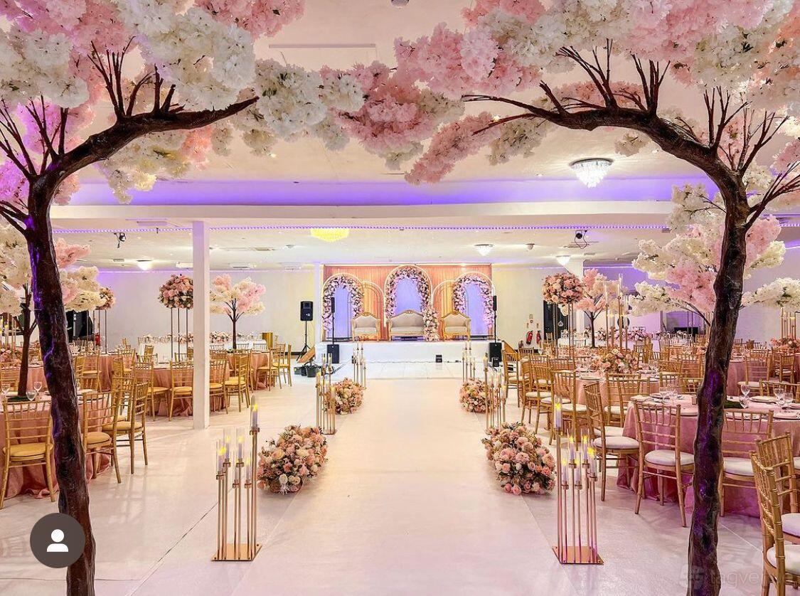 An event venue with faux cherry blossom arches, gold chairs, floral arrangements, and a decorated stage at Kashas Royal.