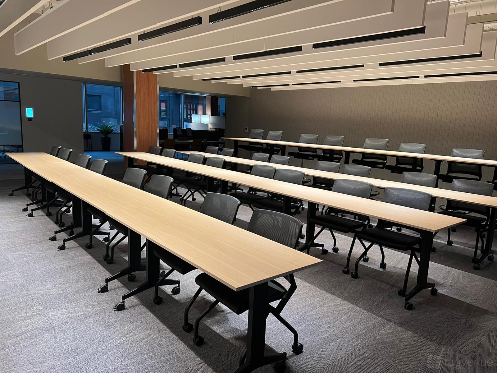 A meeting room with long rectangular tables, mesh chairs, and ceiling light panels at Serendipity Labs Manchester.