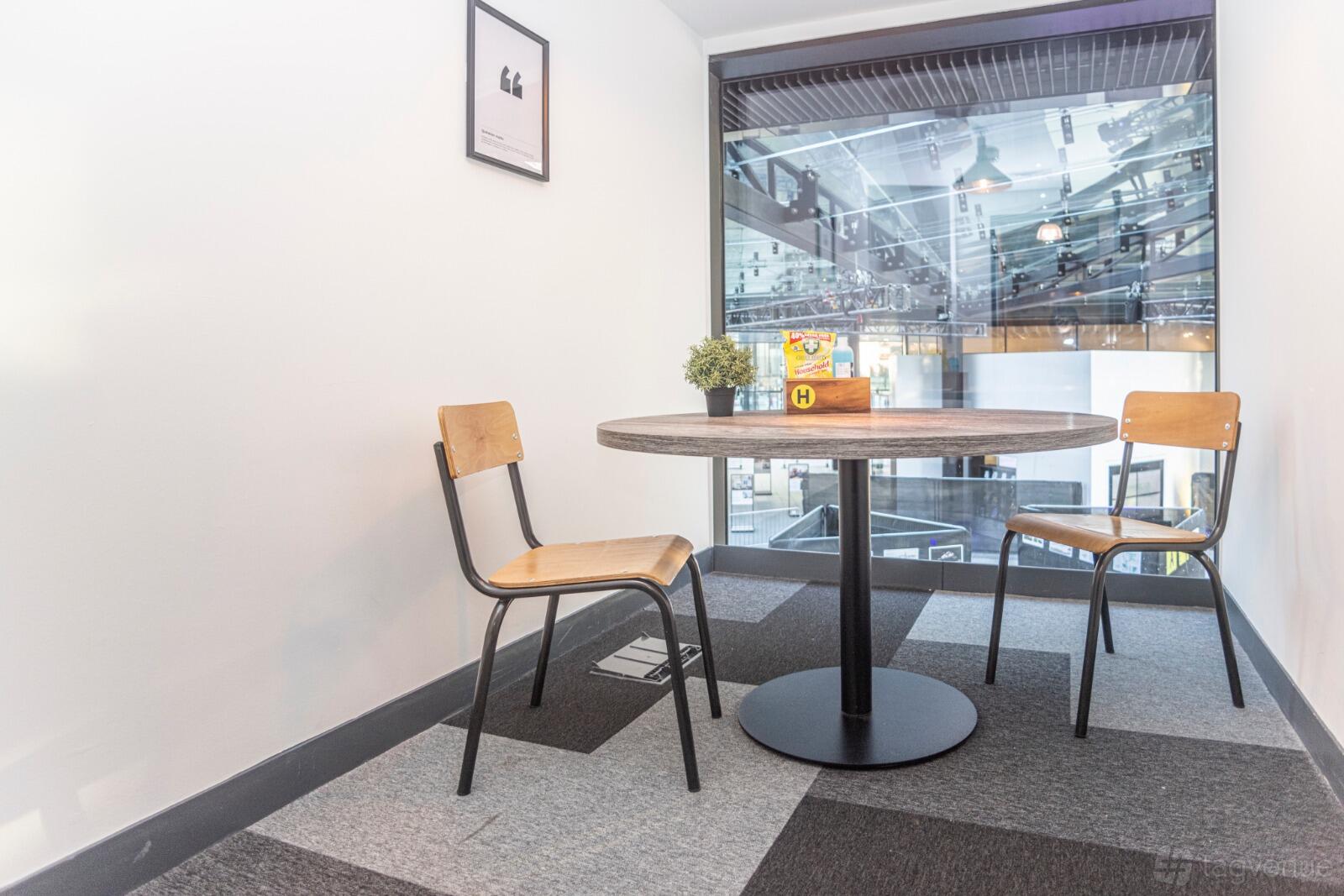 A meeting room with a round table, two wooden chairs, and a glass wall overlooking the building atrium at Avenue HQ Mann Island.