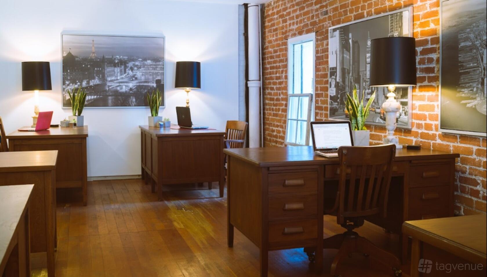 A coworking space with exposed brick walls, wood floors, and vintage desks with lamps at Rita House.