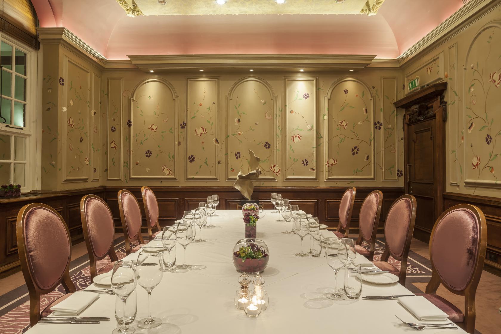 A hotel event room with pink upholstered chairs, floral wall panels, and a long table set for dining at The Roseate Reading.