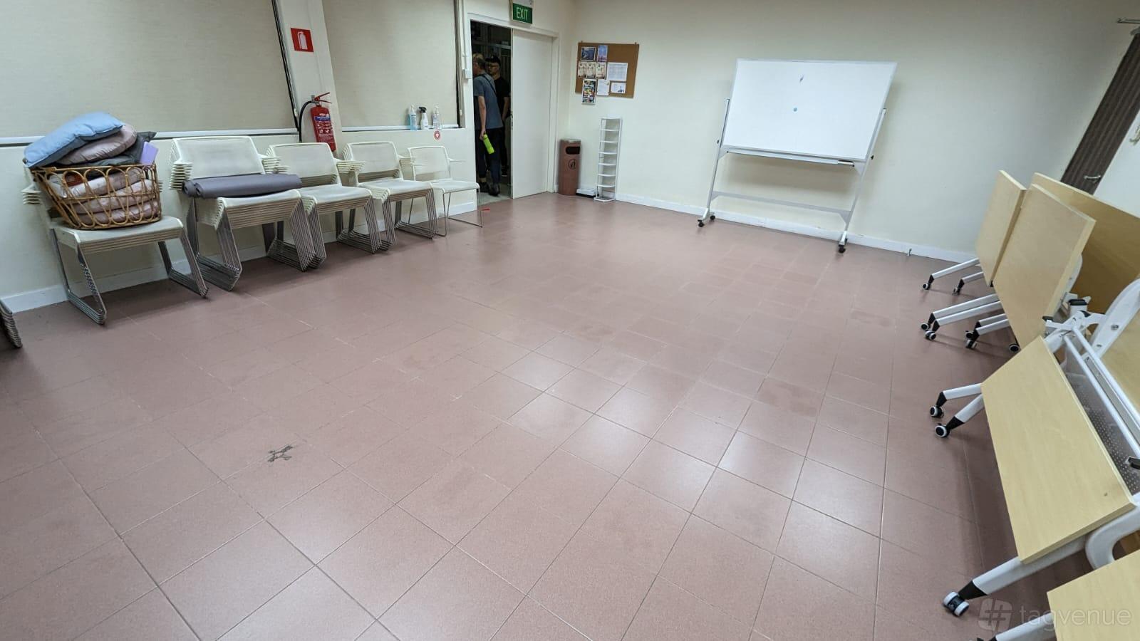 A meeting room with stackable chairs, folding tables, a corkboard, and a whiteboard at We Care Training and Events Space.