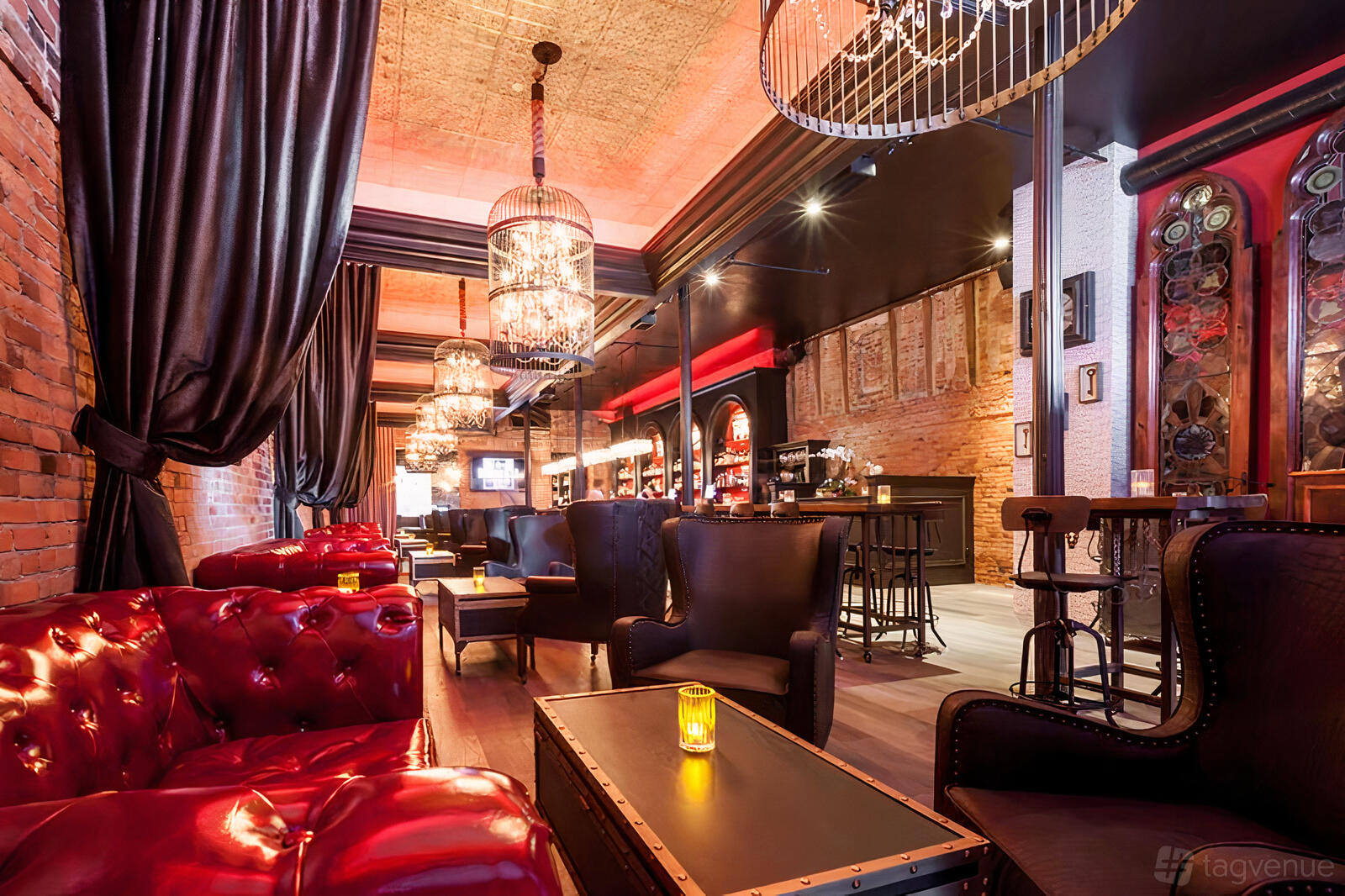A bar with tufted red leather sofas, exposed brick walls, chandeliers, and candlelit tables at Barbarossa Lounge.