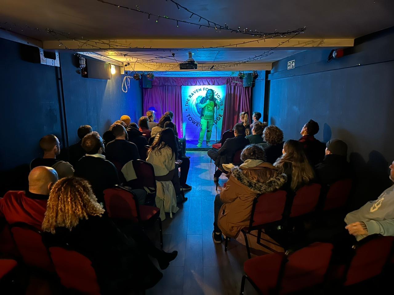 An event space in a pub with a small stage, red theater seating, and string lights at The Raven Tower Bridge.