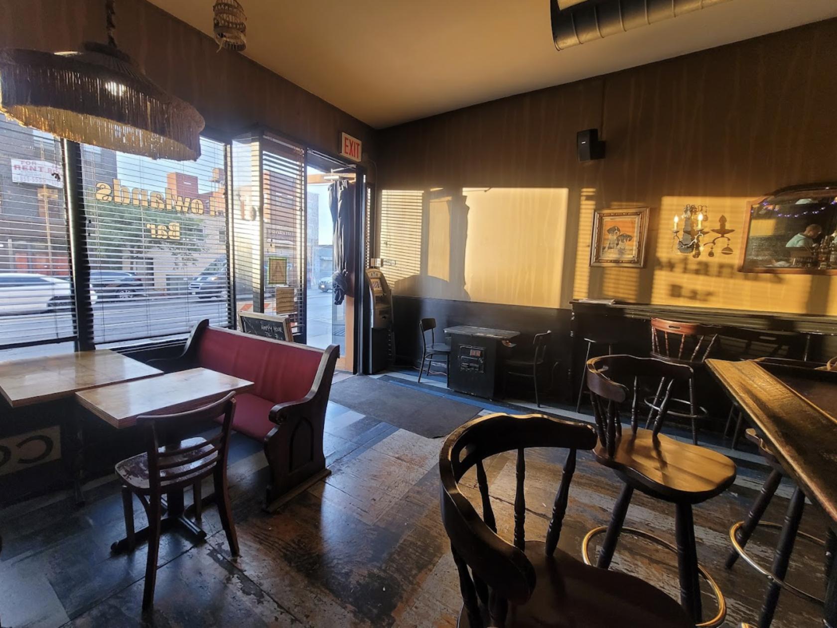 A bar with wooden tables, mixed seating, framed wall art, and natural light from large front windows at Lowlands Bar.