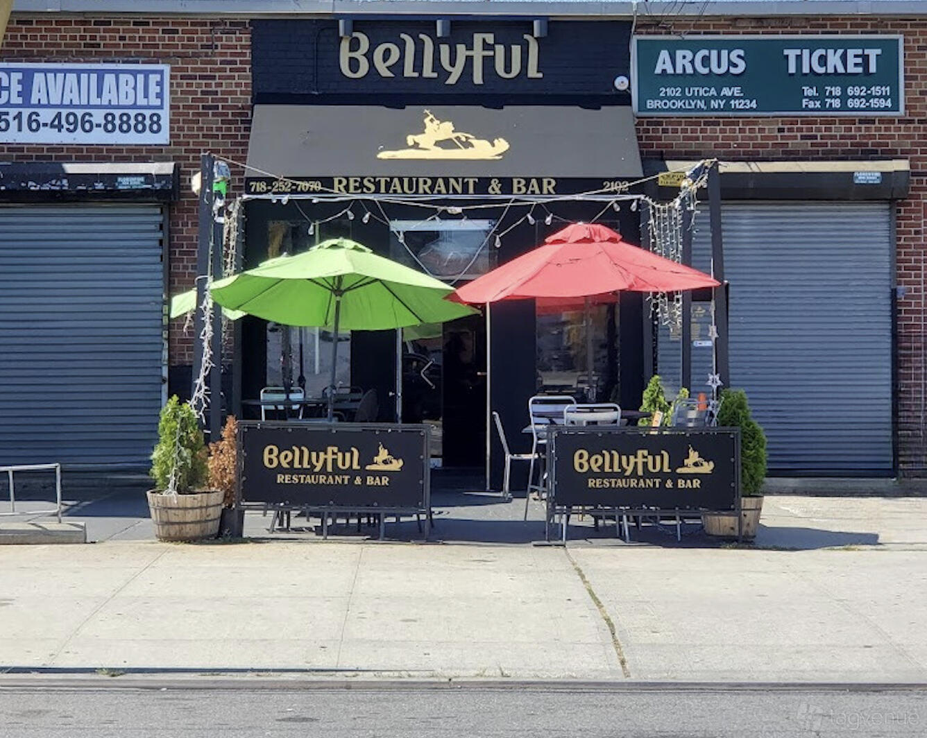 A restaurant with outdoor sidewalk seating, green and red umbrellas, and branded signage at Bellyful Restaurant & Bar.