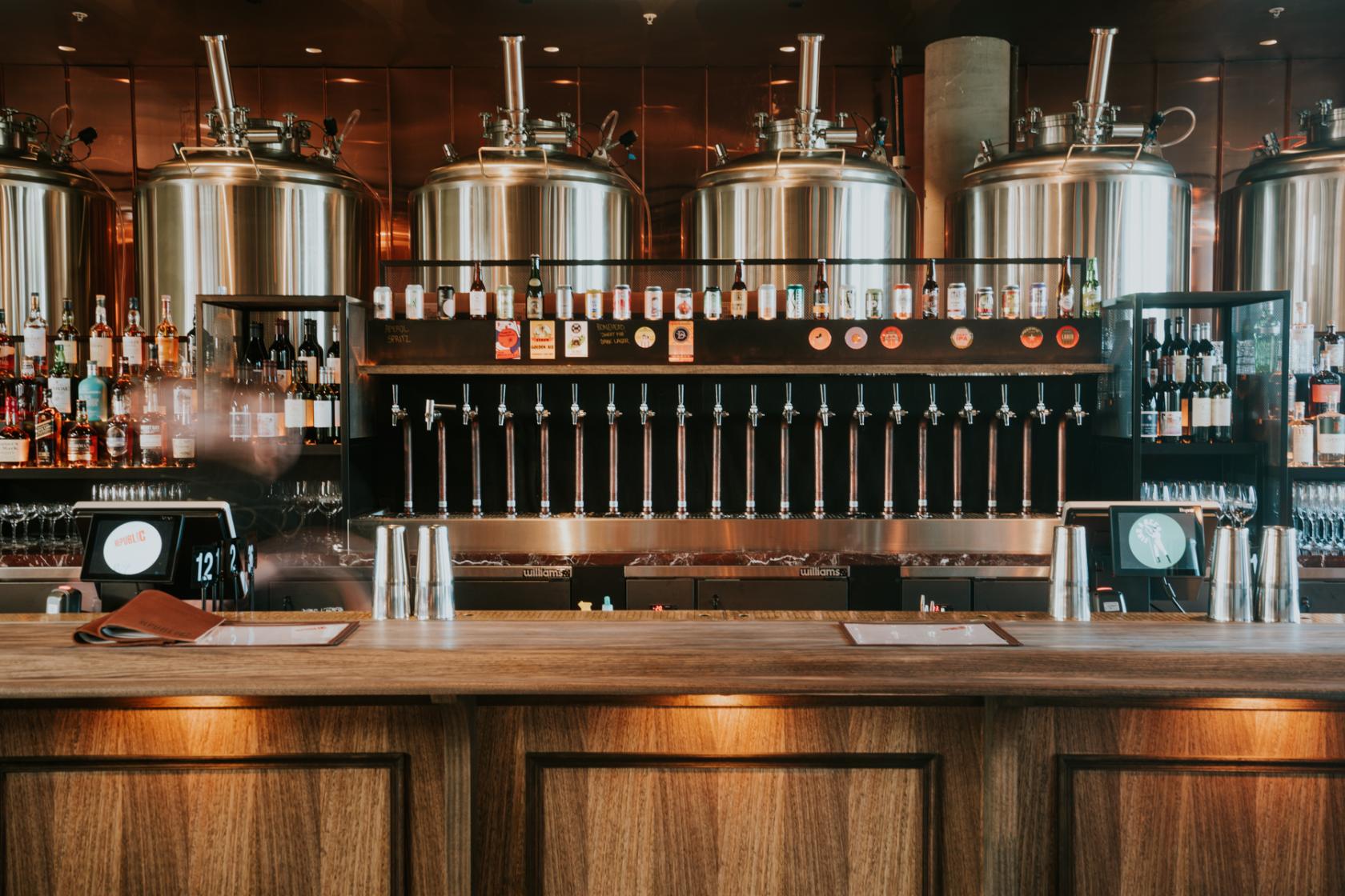 A hotel bar with polished wood counters, rows of beer taps, and large stainless steel brewing tanks at Republic Tavern Brew-Pub.