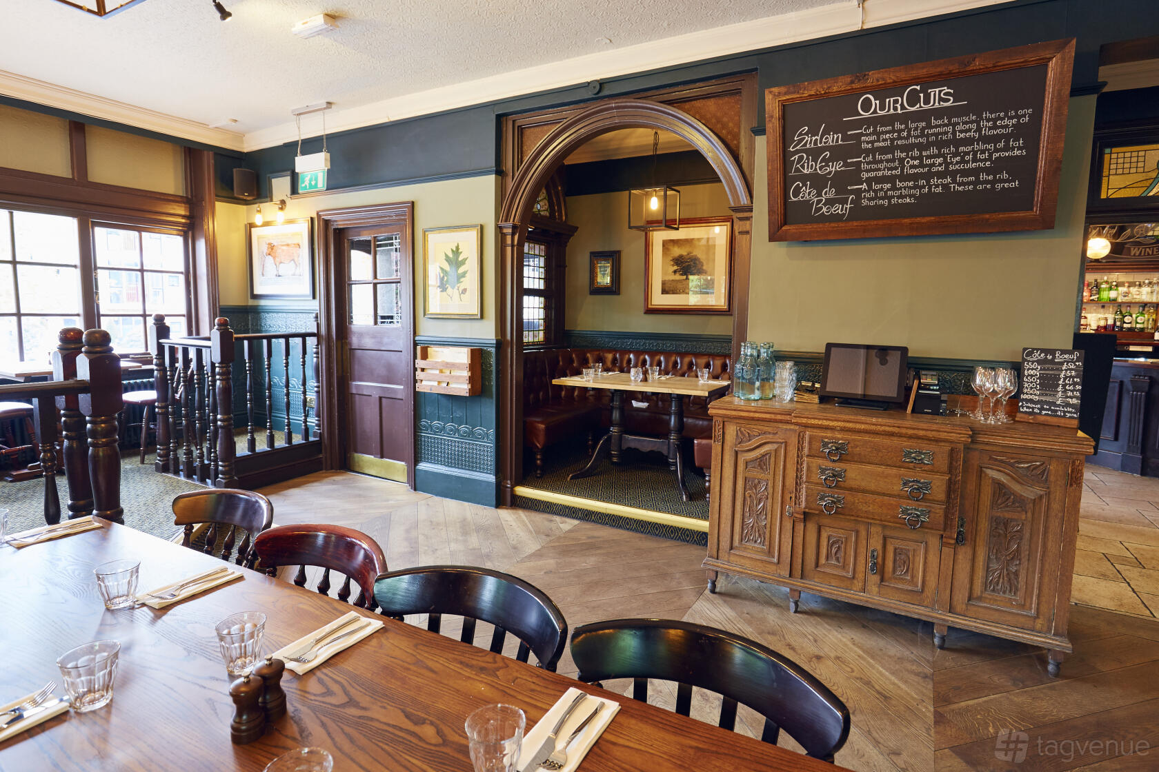 A dining room in a pub with wooden tables set with glassware and cutlery, decorative wall art, and an archway at The Royal Oak.