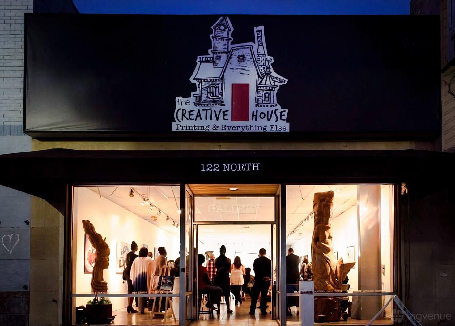 A gallery with large windows, wood sculptures, and an illuminated entrance at The Creative House.