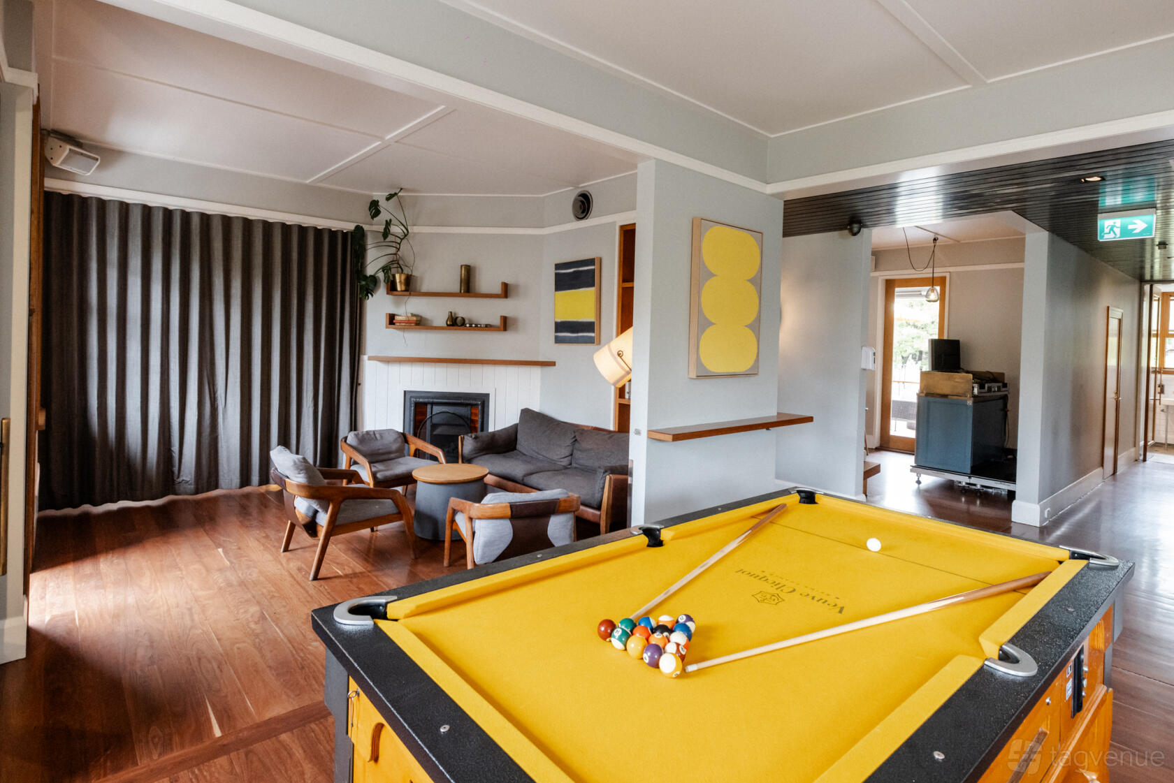 A pub lounge with a yellow pool table, wooden floors, grey sofas, artwork, and a fireplace at The Tilbury Hotel.
