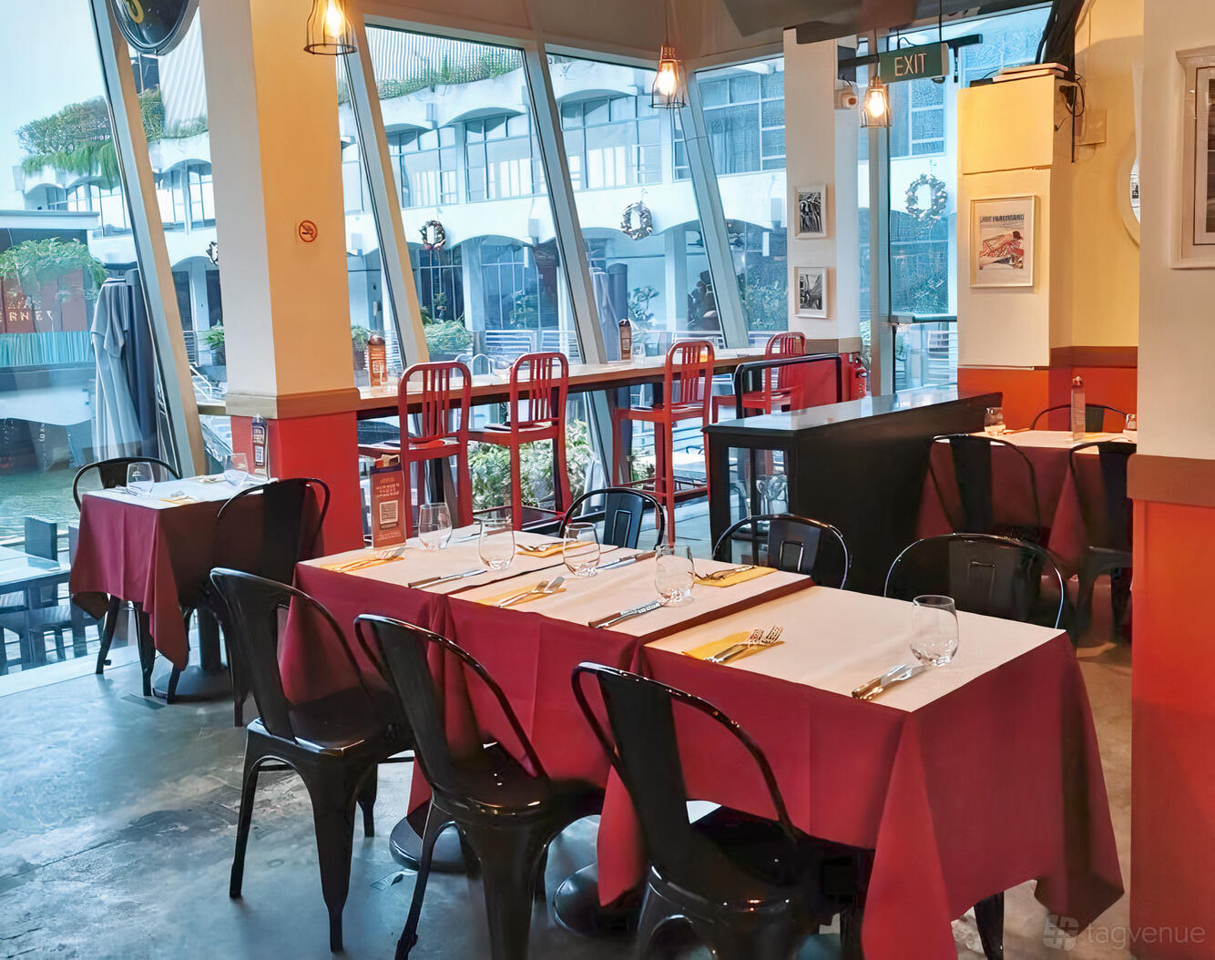 A restaurant with floor-to-ceiling windows, red-accented walls, and tables set with white linens at L’Entrecôte Customs House.