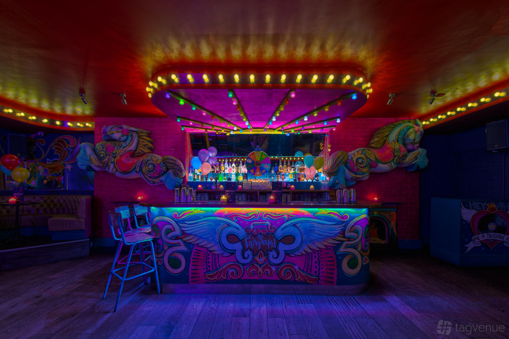 An event space in a bar with neon carnival lights, a colorful mural bar counter, and balloons at Cuckoo.