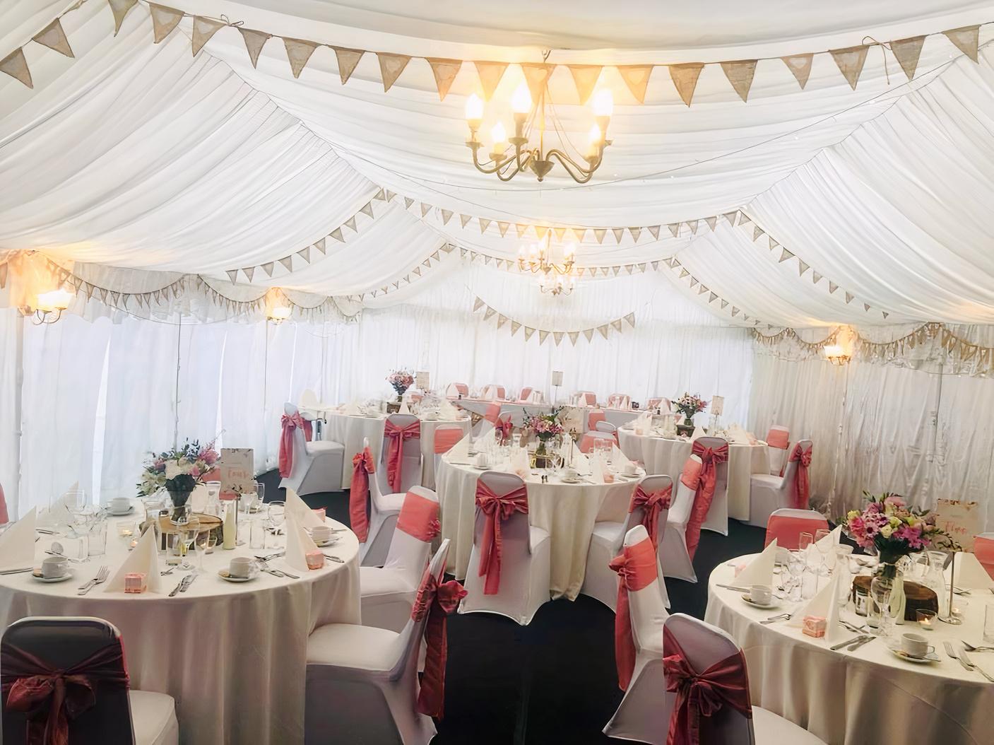 An event space with white draped marquee ceiling, round tables with white linens, and pink chair sashes at Royal Arms Hotel.