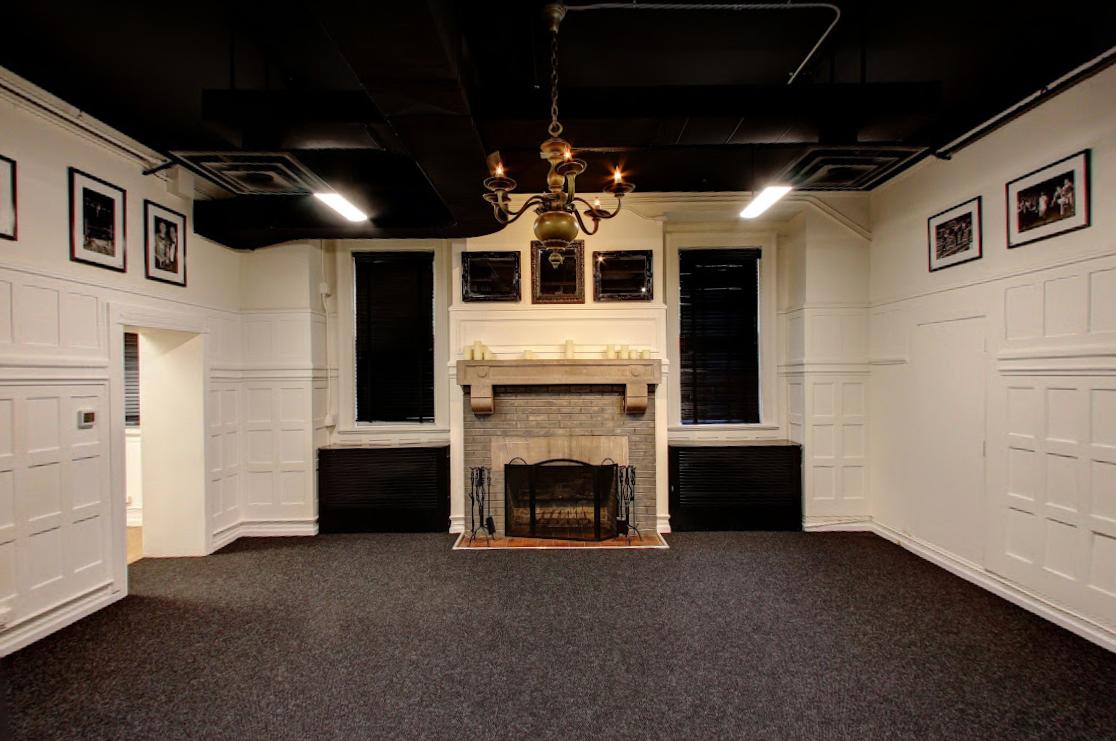 A boardroom with a decorative fireplace, framed photos, paneled white walls, and a brass chandelier at The Armory.