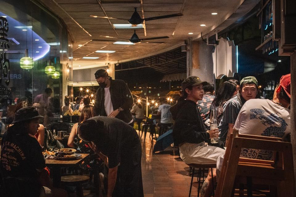 An outdoor space at a bar with wooden tables, string lights, and people dining at Orh Gao Taproom Craft Beer Bar.