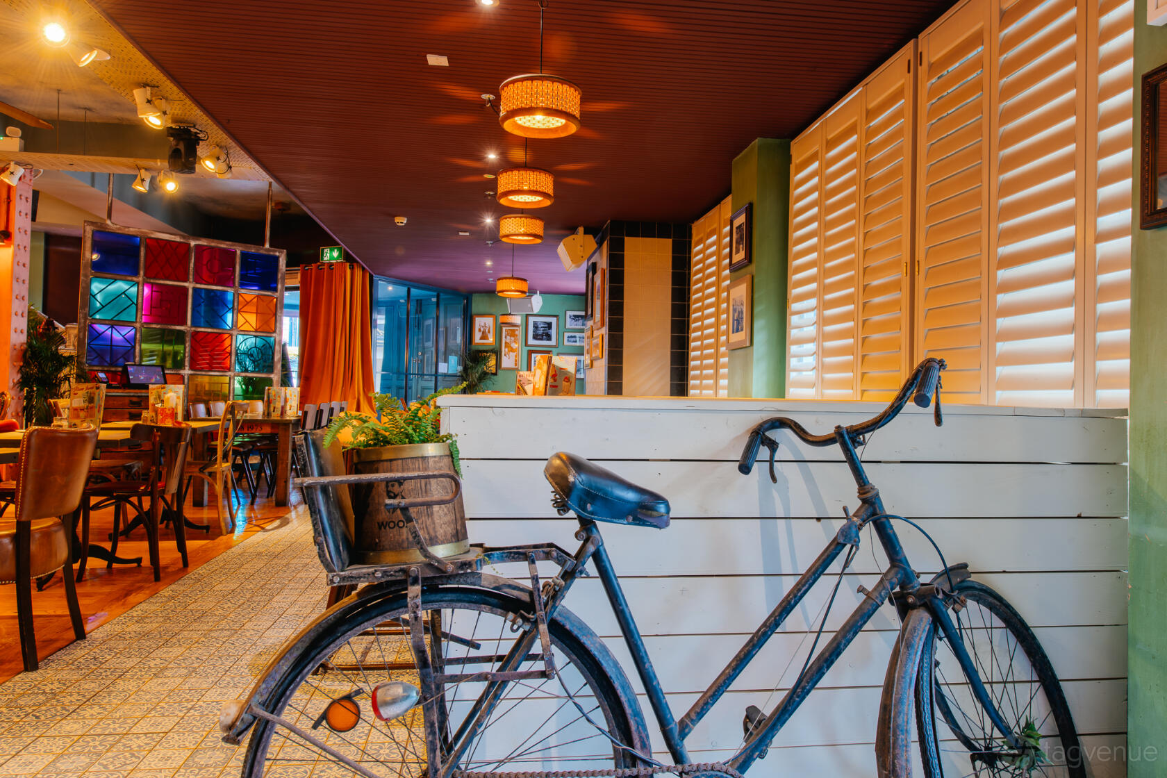 A versatile event space with colorful stained glass windows, vintage bicycle decor, and wooden tables at Revolucion de Cuba Leeds.