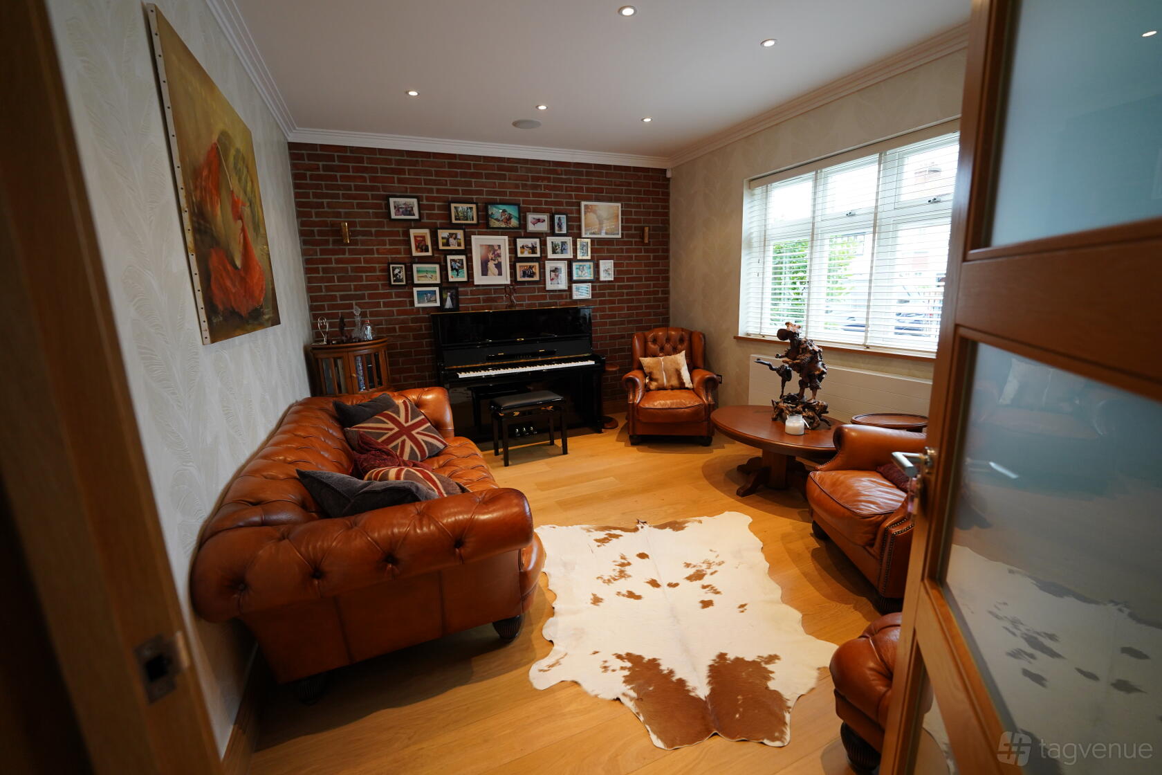 A piano room in a house with a black upright piano, leather sofas, brick accent wall, and a cowhide rug at Luxury piano/music room.