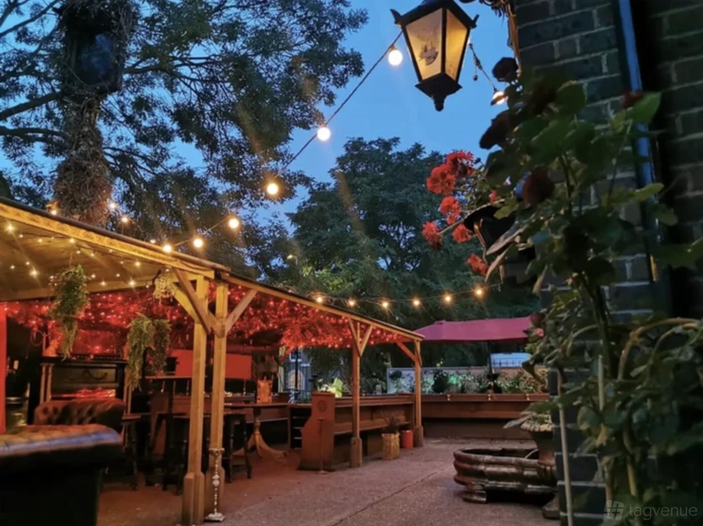 An outdoor pub area with string lights, wooden seating, and potted plants at The Cavendish Arms.