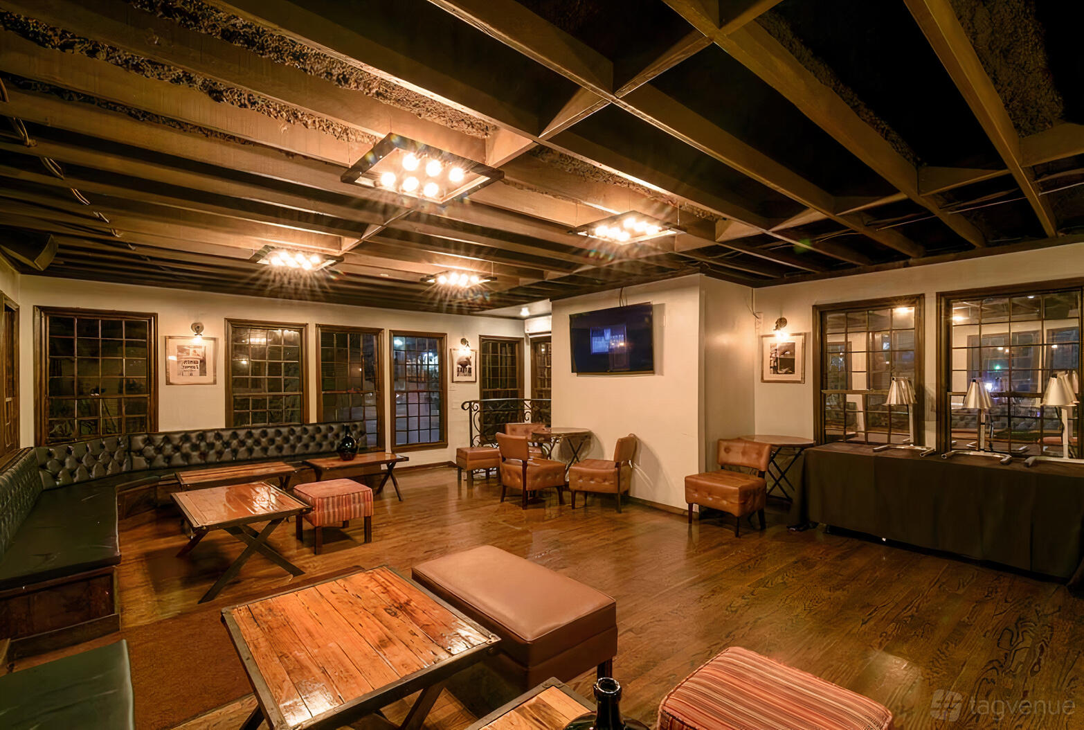 An upstairs event space with wood floors, exposed beams, leather seating, and large windows at Capone's Oven & Bar.