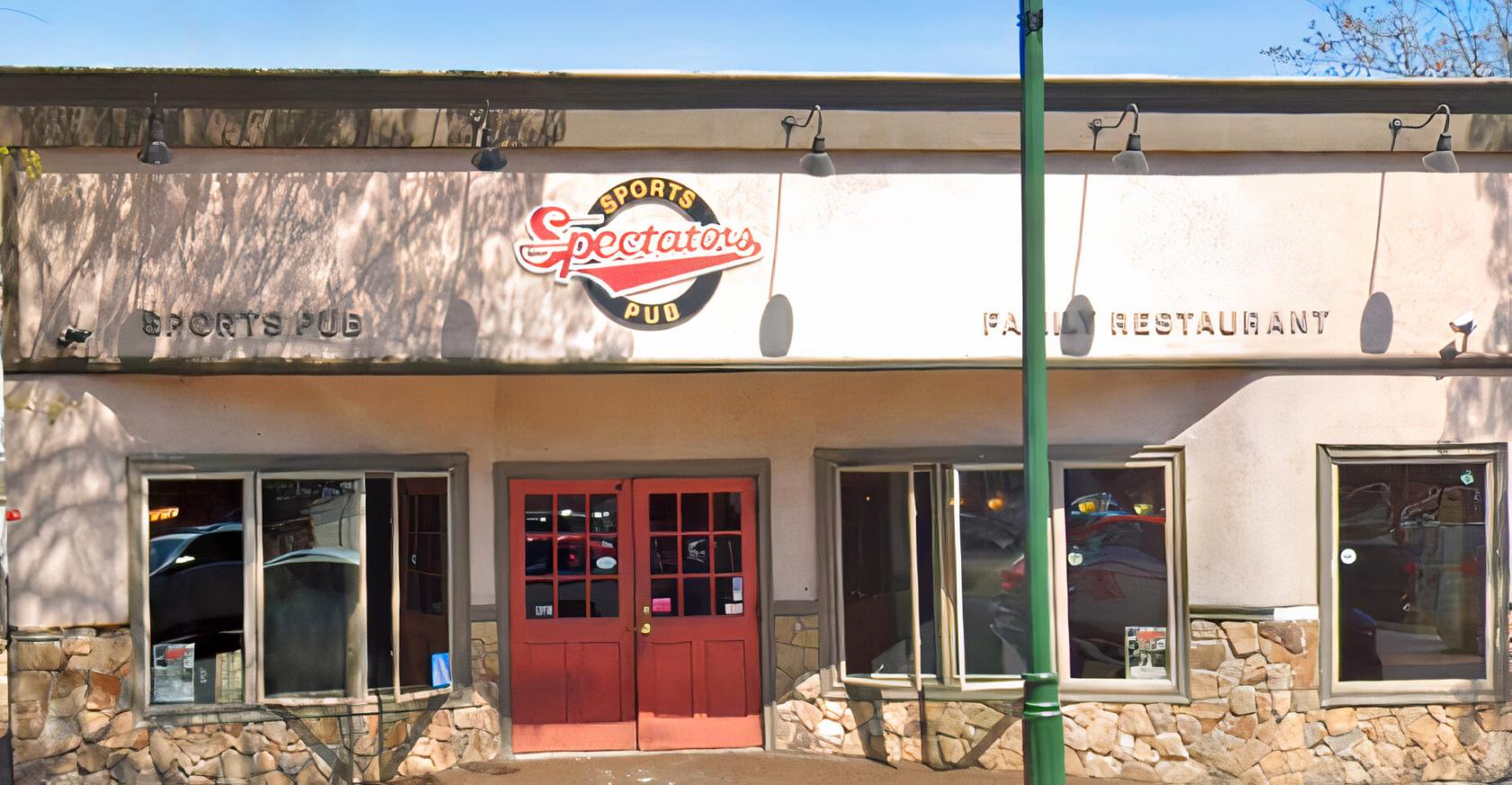 A pub with a stone-accented facade, large windows, and red double doors at Spectators Sports Pub & Restaurant.