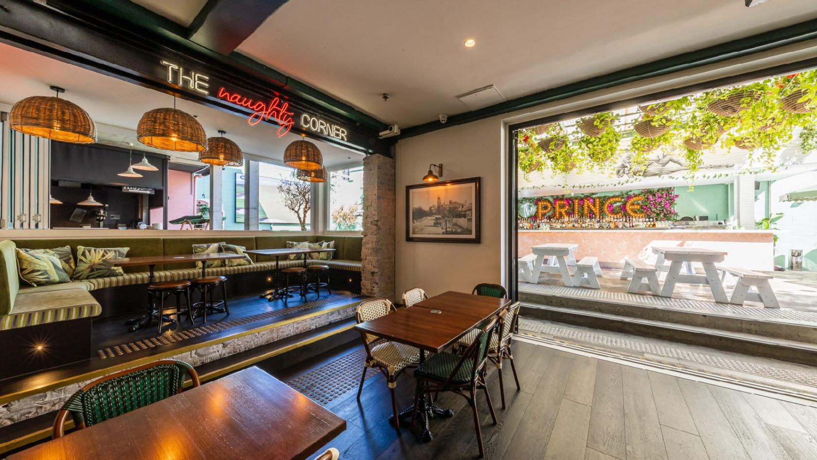 An event space in a pub with rattan pendant lights, wooden tables, and neon signage at The Prince Consort.