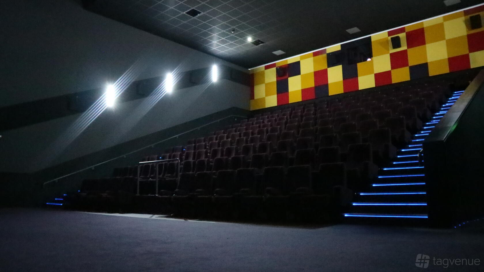 A cinema auditorium with tiered seating, illuminated aisle steps, and a colorful checkerboard back wall at The Light Cinema - Walsall.