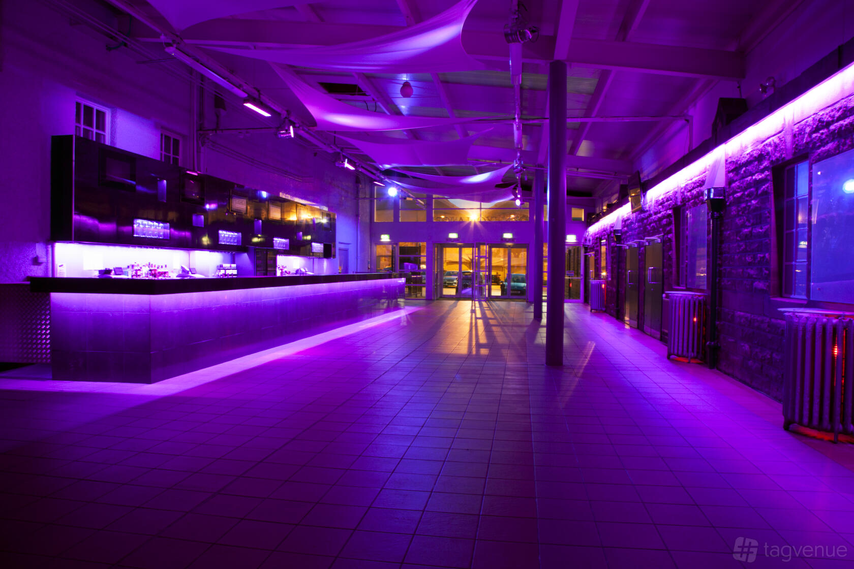 An event venue with a long bar, tiled floors, and purple ambient lighting at Edinburgh Corn Exchange.
