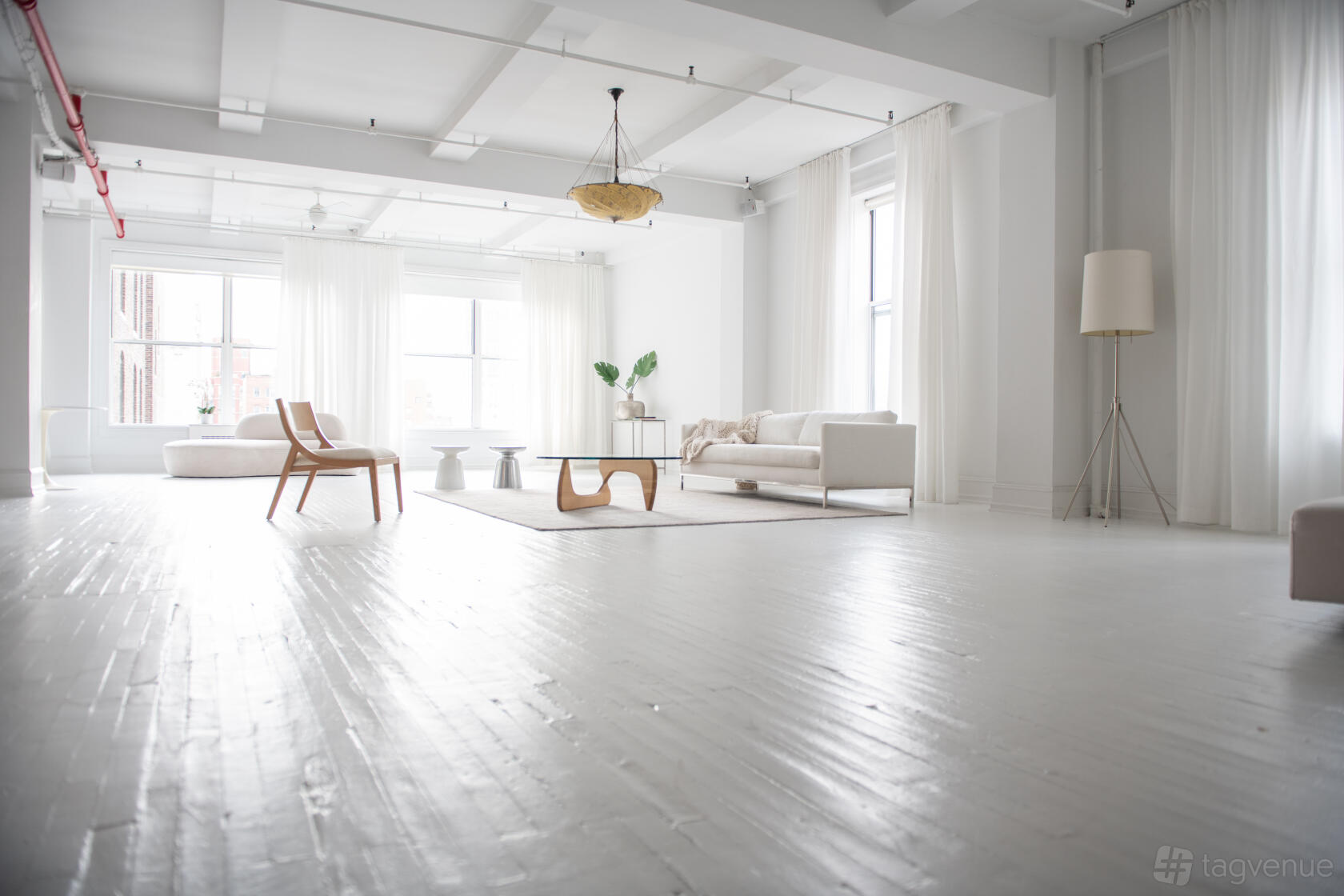 A loft with white painted floors, large windows, sheer curtains, and minimal modern furniture at 24th Street Loft.