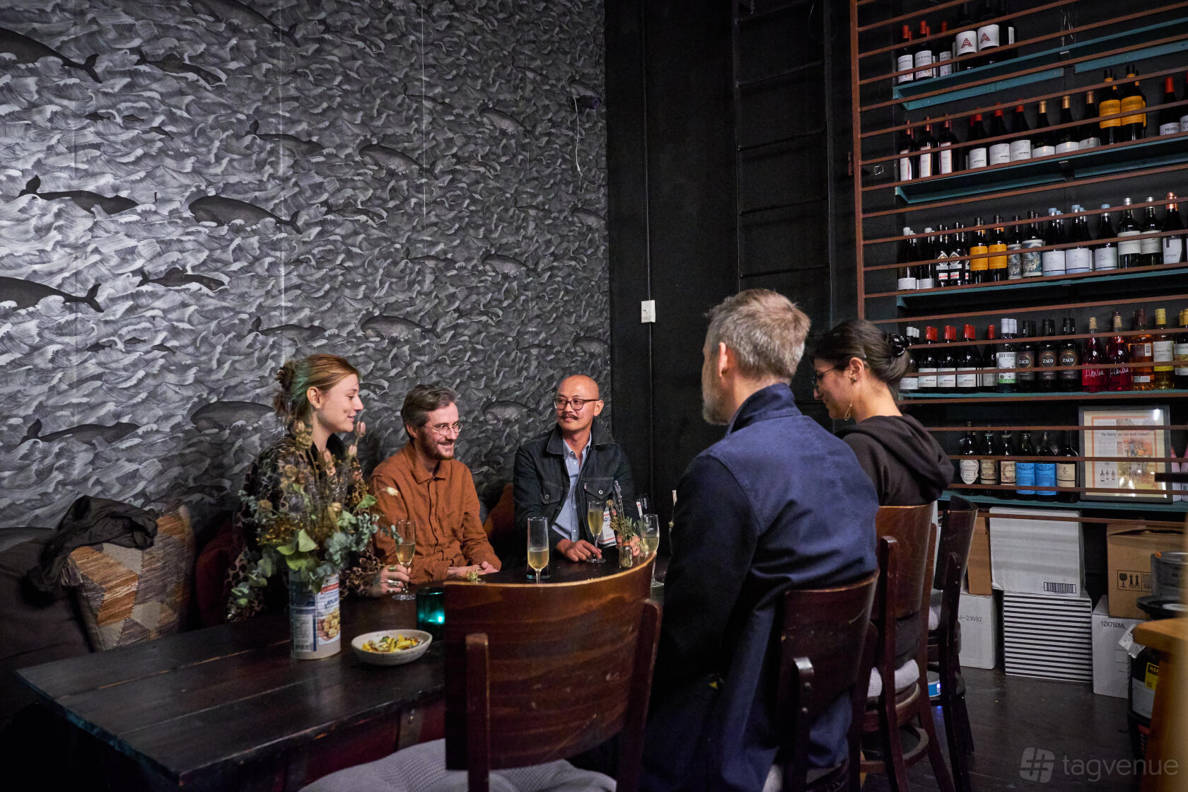 An event space in a bar with a textured whale mural wall, wooden table seating, and shelves stocked with bottles at El Lopo.