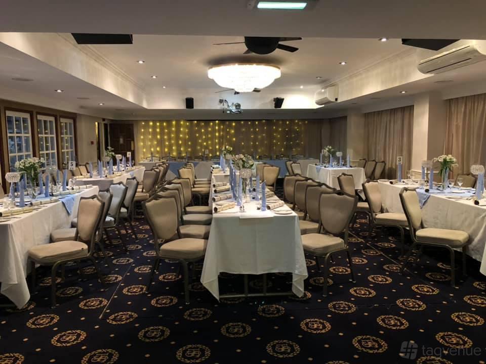 An event space with navy patterned carpeting, banquet tables with white linens, and a backdrop of string lights at Santo's Higham Farm Hotel.