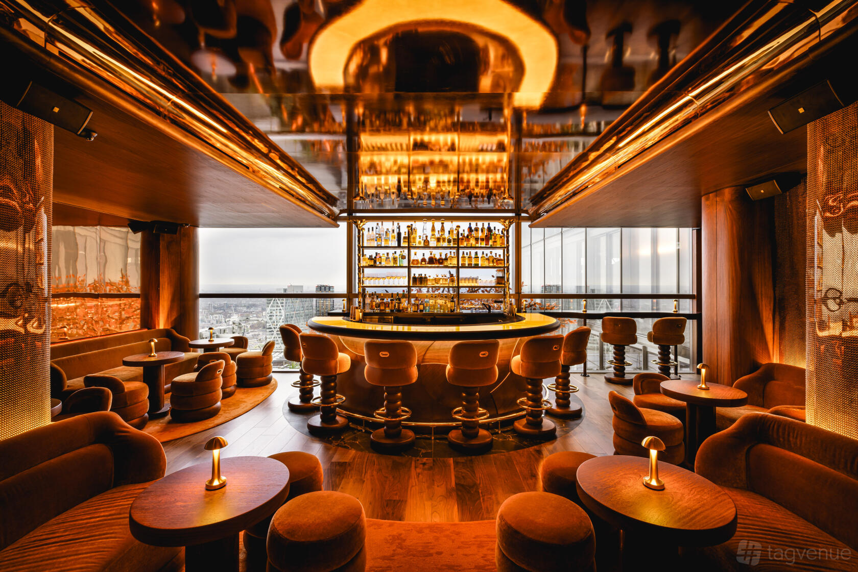 A bar in a restaurant with floor-to-ceiling windows, amber lighting, and velvet lounge seating at SUSHISAMBA.
