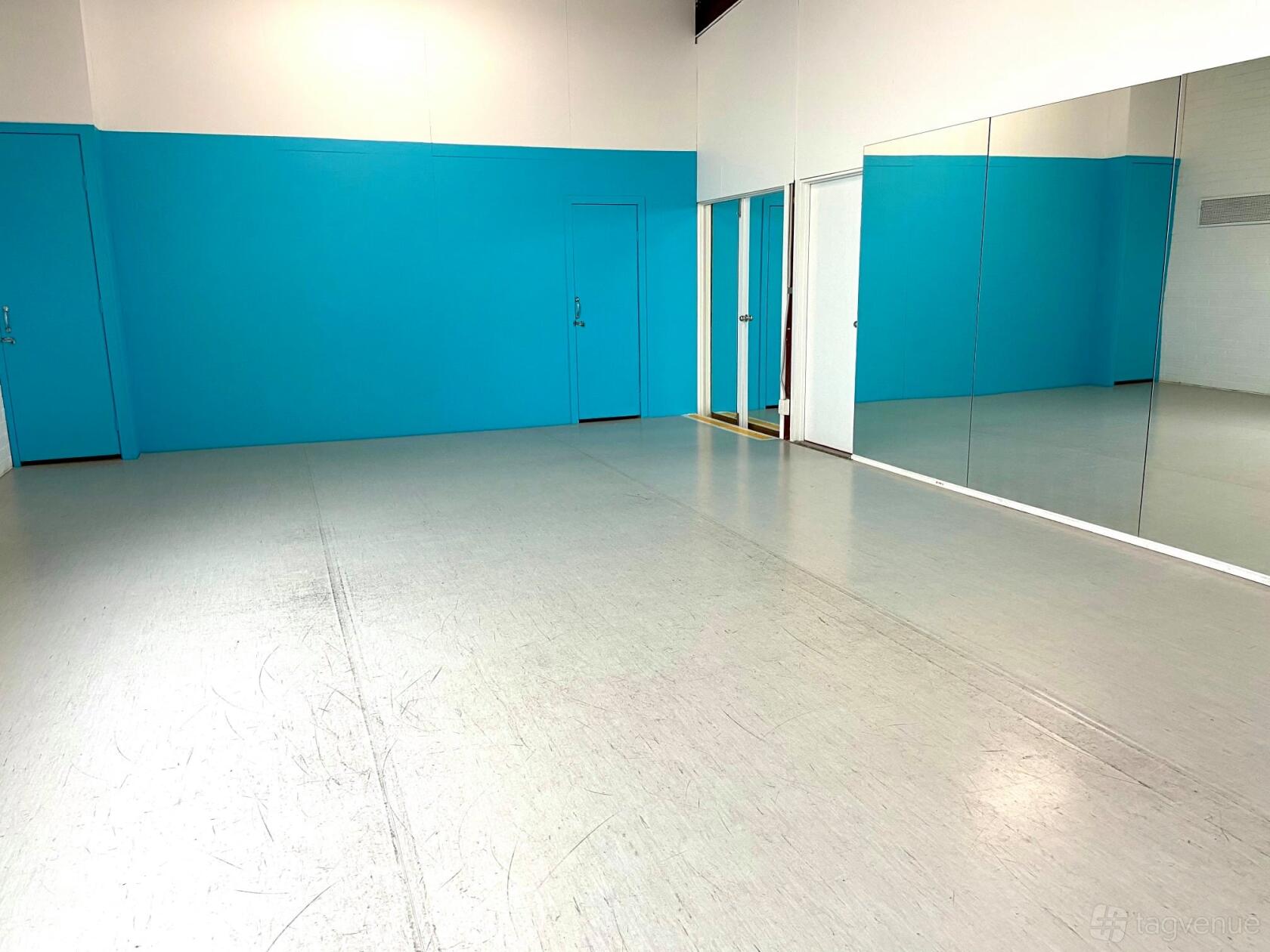 A rehearsal room with a gray sprung floor, bright blue accent wall, and wall-to-wall mirrors at National Performing Arts Company.