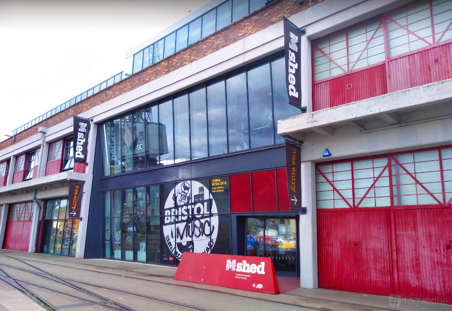 A versatile event space with a glass entrance, red accents, and industrial exterior at M Shed.