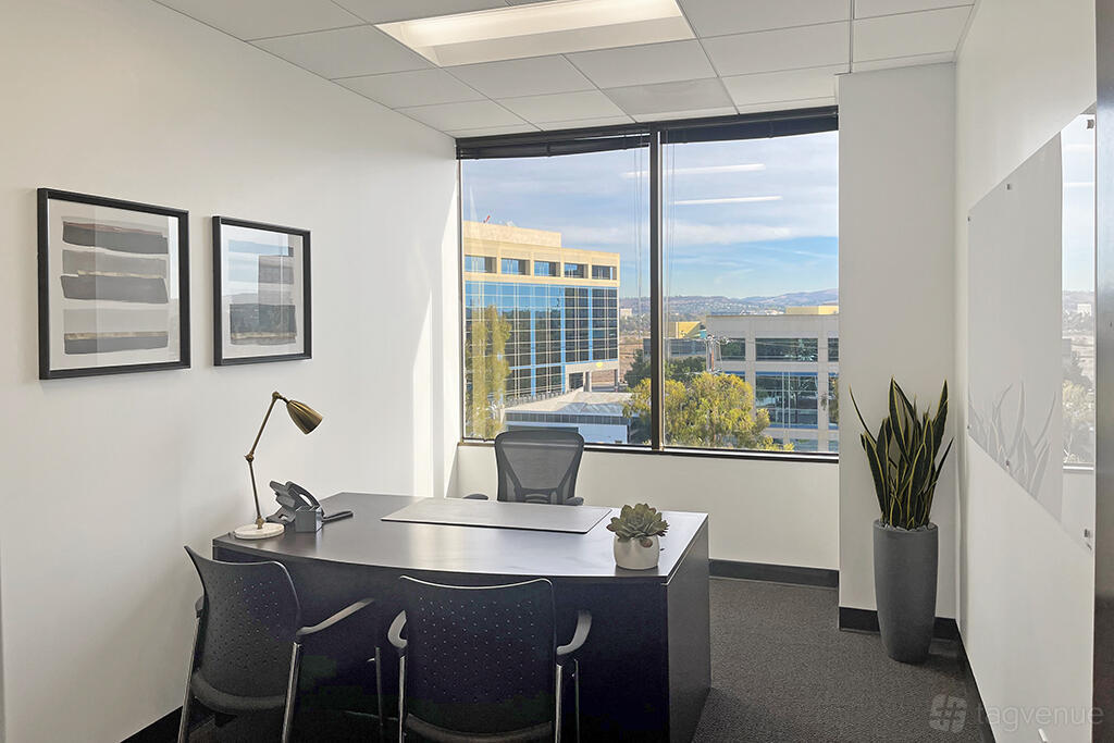 A coworking space with a desk, ergonomic chair, large windows, and minimal decor at Premier Workspaces - 4000 MacArthur Boulevard.