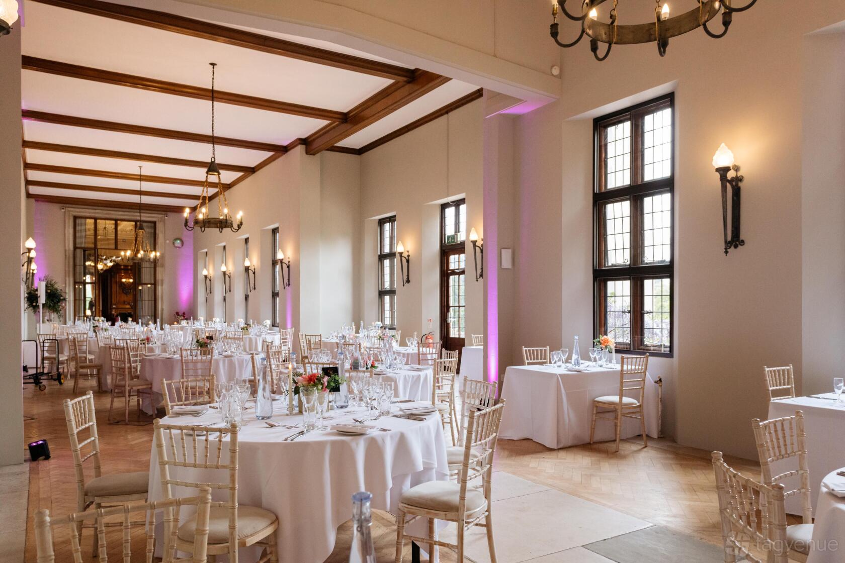 A castle hall with high ceilings, chandeliers, tall windows, and round tables set with white linens at Ashridge House.