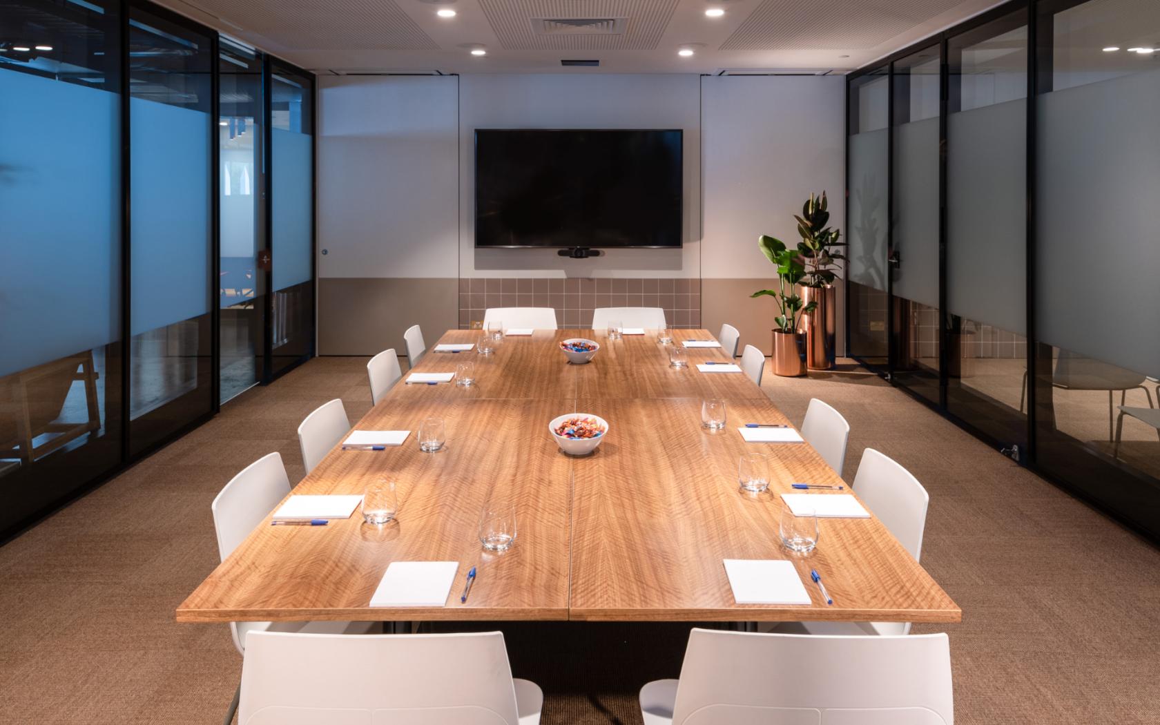 A meeting room with a long wooden table, white chairs, and a large wall-mounted screen at Flex by ISPT at Central Plaza.